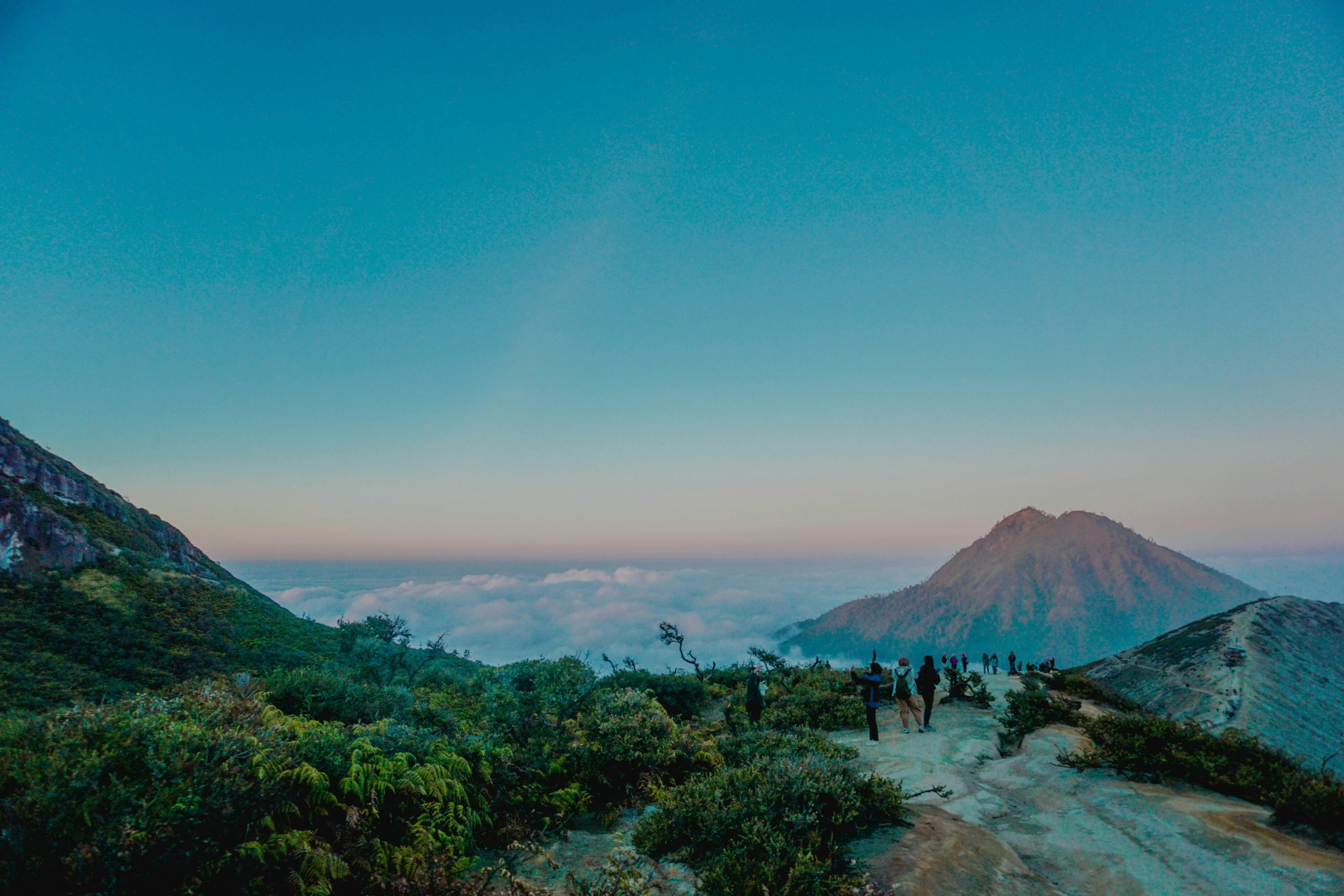 Unrecognizable distant travelers admiring view of picturesque landscape of mountain range with green trees during sunset